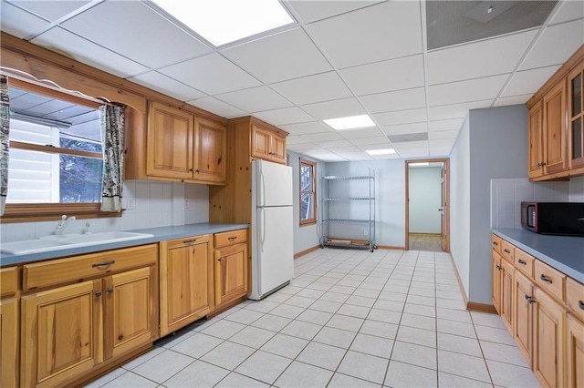 kitchen featuring brown cabinets, light countertops, freestanding refrigerator, a sink, and black microwave