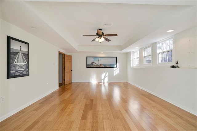 unfurnished living room featuring a tray ceiling, visible vents, light wood-style flooring, and baseboards