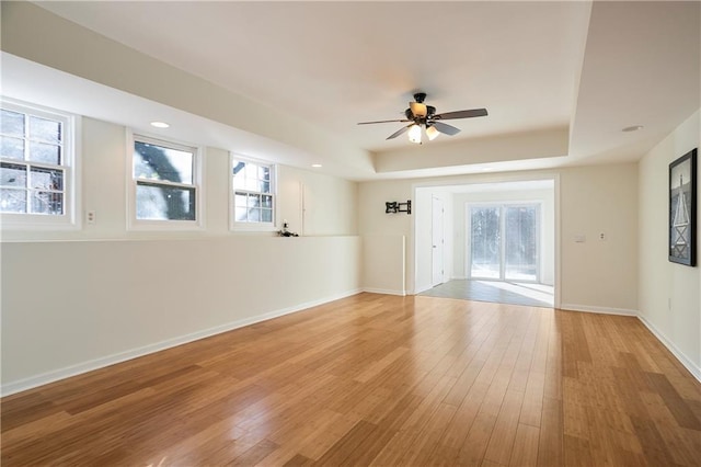 spare room featuring baseboards, a raised ceiling, ceiling fan, light wood-type flooring, and recessed lighting