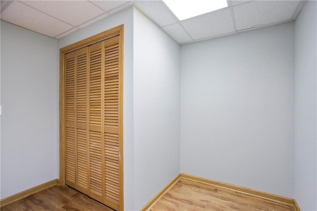 interior space with baseboards, a drop ceiling, and wood finished floors