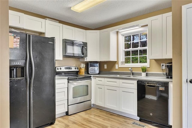 kitchen with light wood-type flooring, a sink, white cabinets, and black appliances