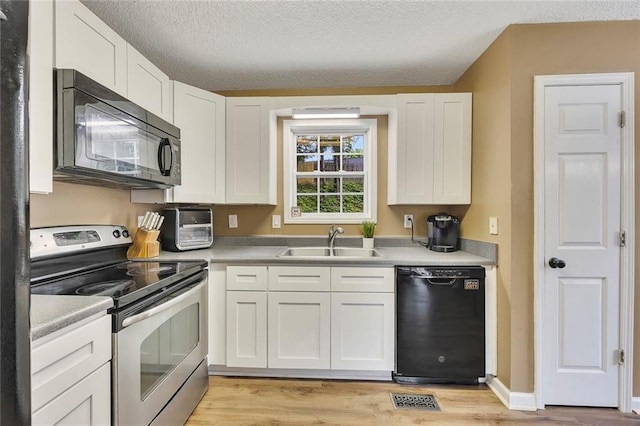 kitchen with a sink, light wood finished floors, white cabinetry, visible vents, and black appliances