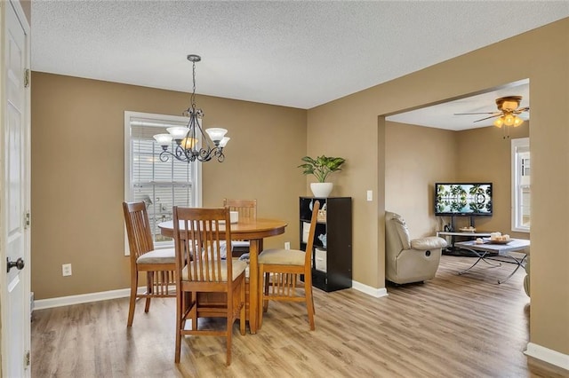 dining space featuring light wood-type flooring, a textured ceiling, baseboards, and ceiling fan with notable chandelier