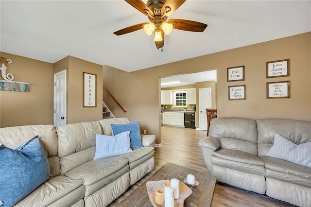living area featuring light wood finished floors, ceiling fan, and stairway