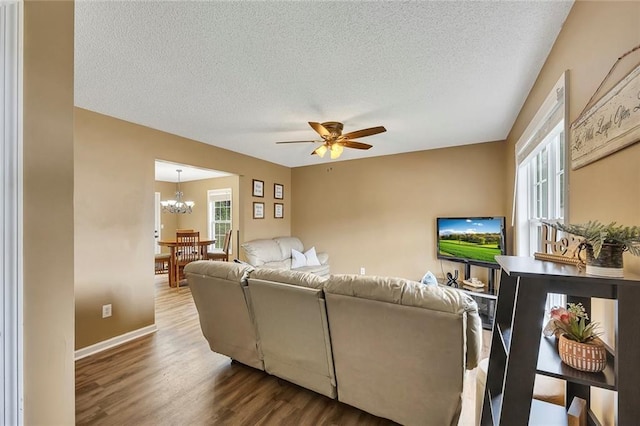 living area featuring baseboards, a textured ceiling, wood finished floors, and ceiling fan with notable chandelier