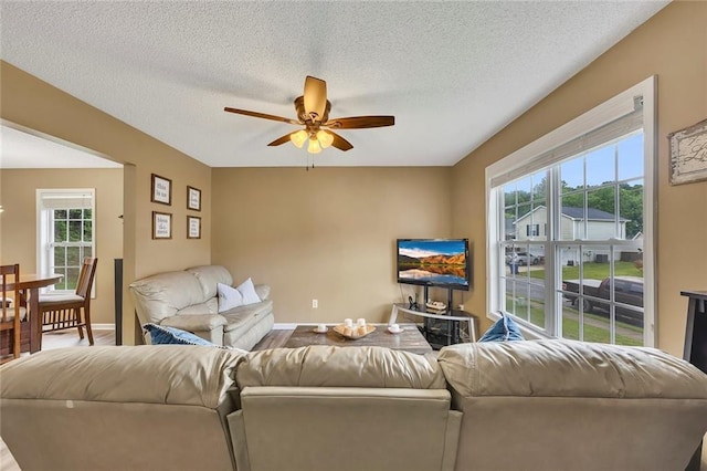 living area with baseboards, a ceiling fan, a textured ceiling, and a healthy amount of sunlight