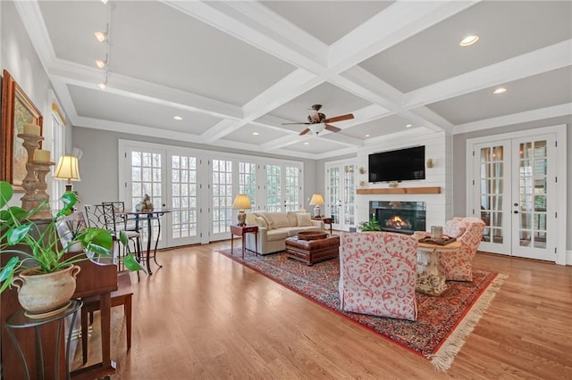 living area featuring beam ceiling, coffered ceiling, a warm lit fireplace, wood finished floors, and french doors