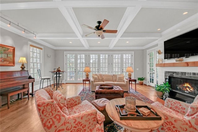 living area with a wealth of natural light, coffered ceiling, a warm lit fireplace, and ceiling fan