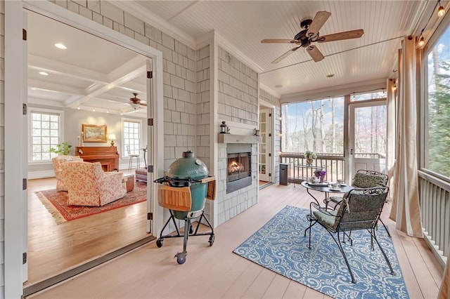 sunroom featuring beam ceiling, coffered ceiling, a warm lit fireplace, and ceiling fan