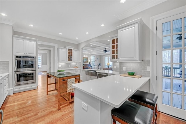 kitchen with ceiling fan, appliances with stainless steel finishes, a peninsula, light wood-style floors, and white cabinetry