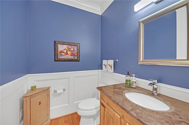 bathroom featuring a wainscoted wall, toilet, ornamental molding, a decorative wall, and vanity