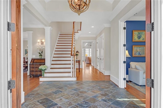 entrance foyer with baseboards, stairway, ornamental molding, stone tile floors, and an inviting chandelier