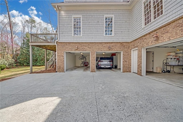 view of side of property featuring brick siding, an attached garage, concrete driveway, and stairs