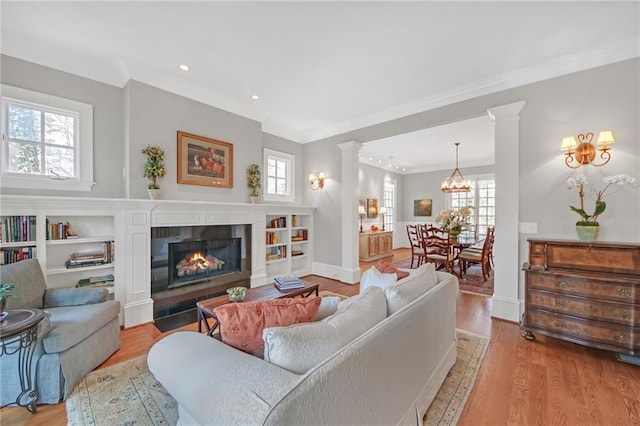 living room featuring a fireplace with flush hearth, a healthy amount of sunlight, decorative columns, and wood finished floors