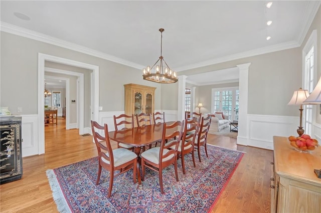 dining room featuring decorative columns, light wood-style floors, wainscoting, and a chandelier