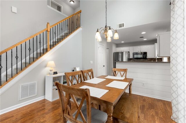 dining room featuring dark wood-type flooring, a towering ceiling, and an inviting chandelier