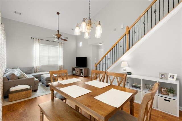 dining space featuring hardwood / wood-style flooring, ceiling fan with notable chandelier, and high vaulted ceiling