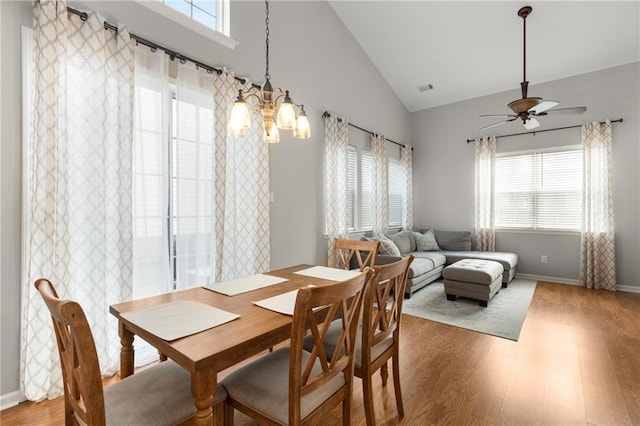 dining room with high vaulted ceiling, wood-type flooring, and ceiling fan with notable chandelier