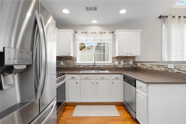 kitchen with sink, white cabinetry, light hardwood / wood-style flooring, appliances with stainless steel finishes, and backsplash