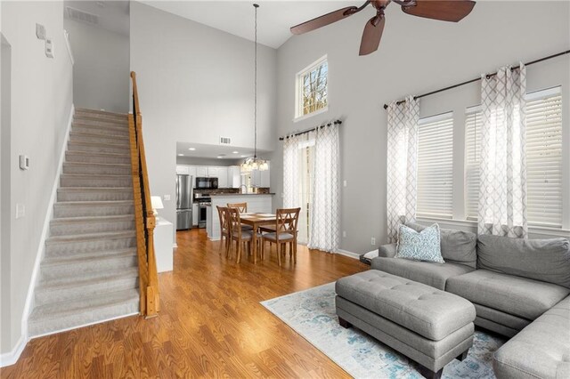 living room with ceiling fan with notable chandelier, a towering ceiling, and light hardwood / wood-style floors