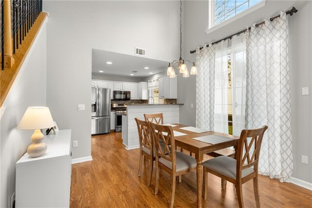 dining space featuring a towering ceiling, sink, light hardwood / wood-style flooring, and a notable chandelier