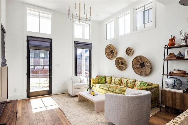 living area with baseboards, a high ceiling, hardwood / wood-style floors, and an inviting chandelier