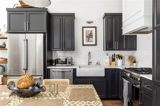 kitchen featuring decorative backsplash, high end appliances, light countertops, dark cabinetry, and a sink