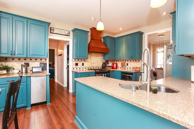 kitchen featuring stainless steel appliances, a sink, hanging light fixtures, blue cabinetry, and custom exhaust hood