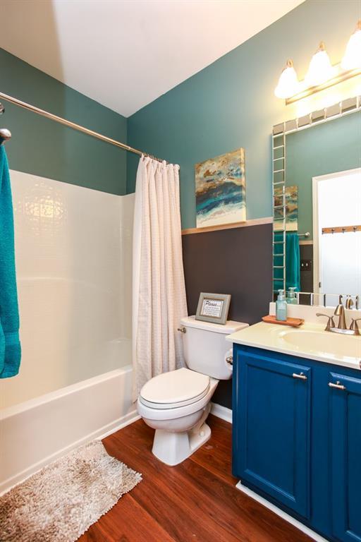 bathroom with toilet, vanity, wood finished floors, and shower / bath combo with shower curtain