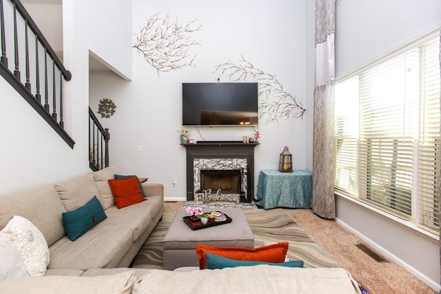 carpeted living area featuring a fireplace, a towering ceiling, baseboards, and stairs