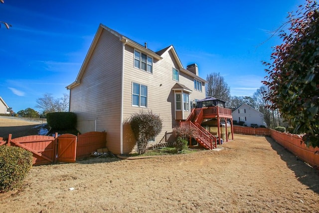 rear view of property featuring a deck, fence, stairway, a gate, and a chimney