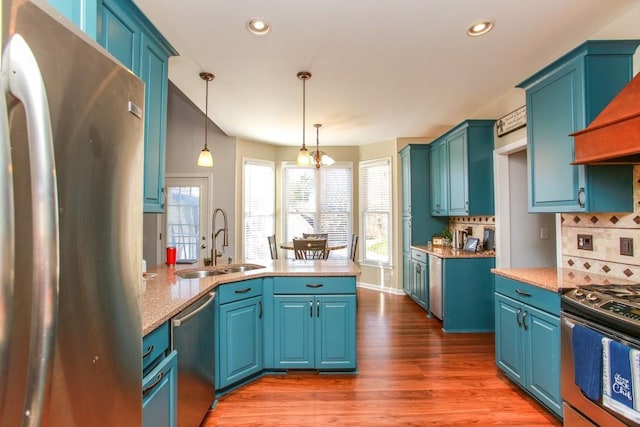 kitchen with dark wood-type flooring, hanging light fixtures, blue cabinets, stainless steel appliances, and a sink