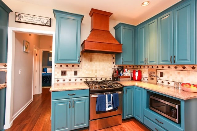 kitchen featuring dark wood finished floors, tasteful backsplash, appliances with stainless steel finishes, blue cabinets, and premium range hood