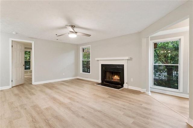 unfurnished living room with a ceiling fan, light wood-type flooring, a fireplace, and baseboards