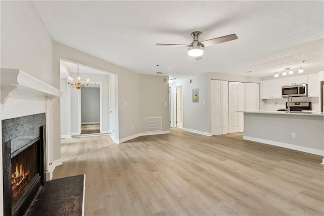 unfurnished living room with visible vents, light wood-style flooring, a fireplace with flush hearth, baseboards, and ceiling fan with notable chandelier