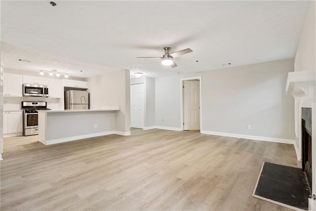 unfurnished living room featuring light wood-style floors, a fireplace with flush hearth, baseboards, and ceiling fan