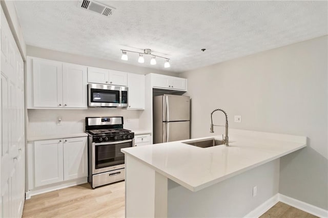 kitchen with light countertops, appliances with stainless steel finishes, white cabinetry, a sink, and a peninsula