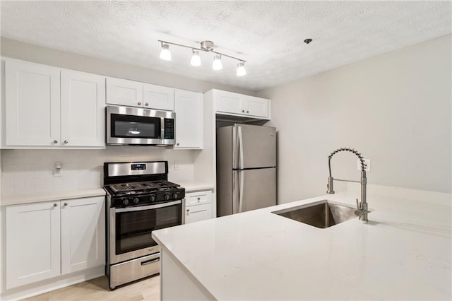 kitchen featuring a textured ceiling, stainless steel appliances, a sink, white cabinetry, and light countertops