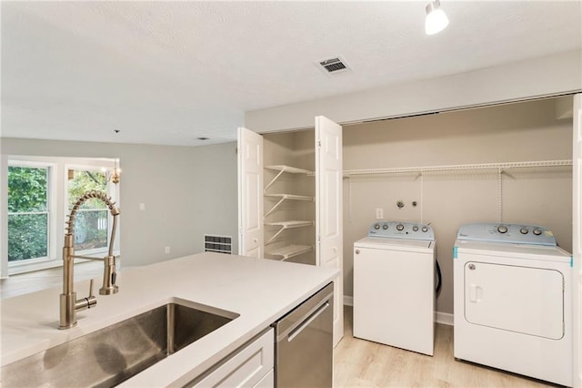 clothes washing area featuring light wood finished floors, visible vents, a sink, separate washer and dryer, and laundry area