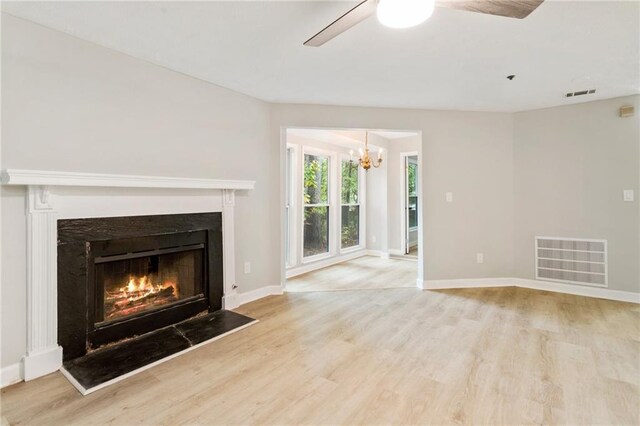 unfurnished living room with a warm lit fireplace, visible vents, light wood finished floors, and ceiling fan with notable chandelier