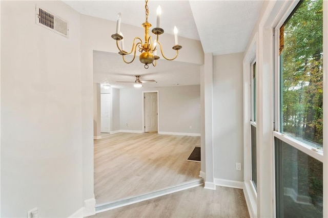 spare room featuring light wood-style floors, visible vents, baseboards, and ceiling fan with notable chandelier