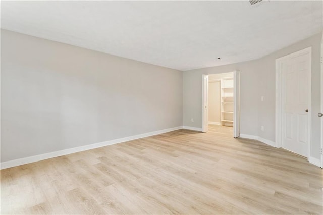 unfurnished bedroom featuring light wood-style floors, a spacious closet, baseboards, and a closet