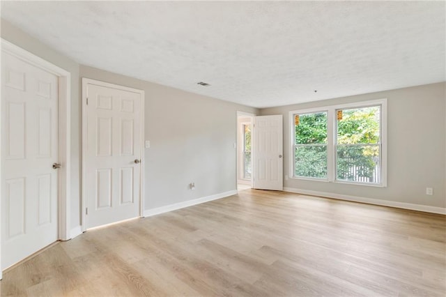 unfurnished room featuring light wood-type flooring, visible vents, and baseboards