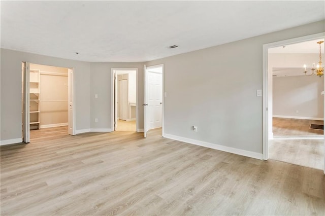 unfurnished bedroom featuring a walk in closet, a closet, an inviting chandelier, light wood-type flooring, and baseboards