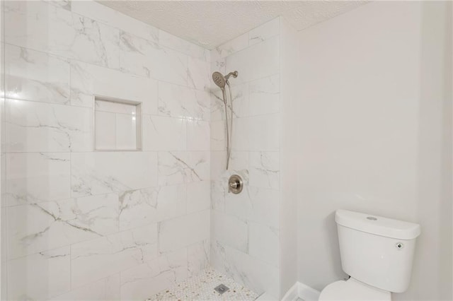 bathroom with a textured ceiling, tiled shower, and toilet