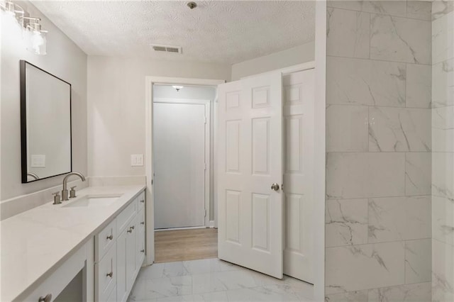 bathroom with marble finish floor, visible vents, a textured ceiling, and vanity