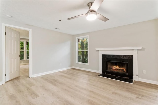 unfurnished living room featuring ceiling fan, light wood finished floors, a premium fireplace, and baseboards