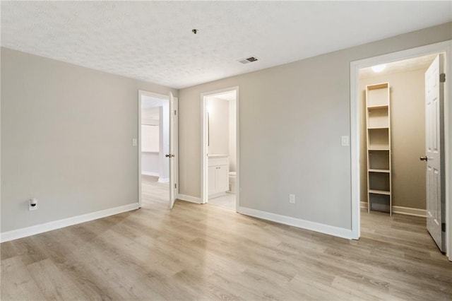 unfurnished bedroom with light wood finished floors, a walk in closet, and visible vents