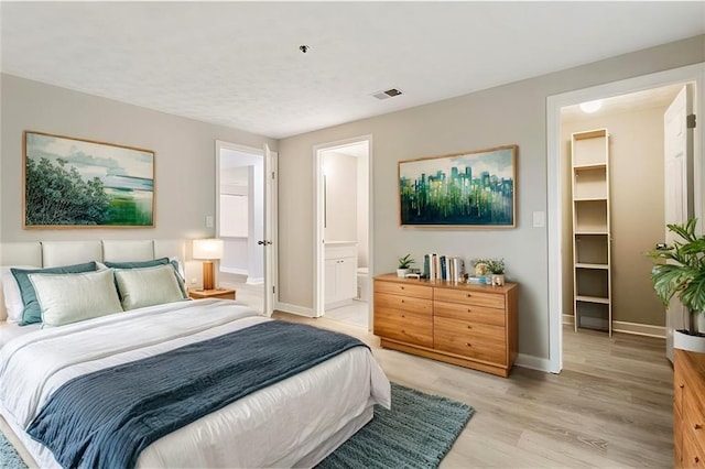bedroom with a walk in closet, light wood finished floors, visible vents, connected bathroom, and baseboards