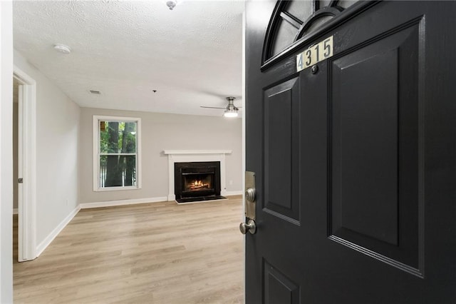 interior space with a textured ceiling, baseboards, a fireplace with flush hearth, and light wood-style floors